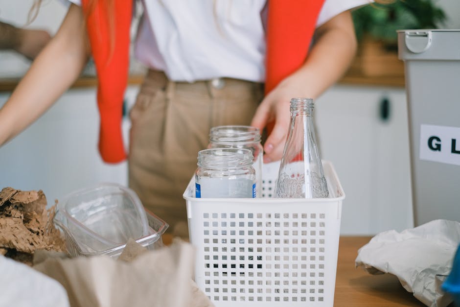 A clear plastic bag filled with several empty, transparent plastic bottles, dominated by bottle caps and necks, being held by a person wearing a yellow jacket, set against a blurred background with a 